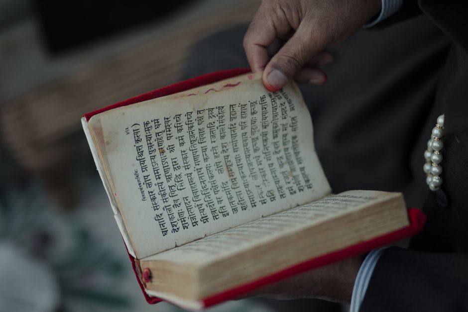 A hand holding an ancient book with Sanskrit text, symbolizing cultural heritage.